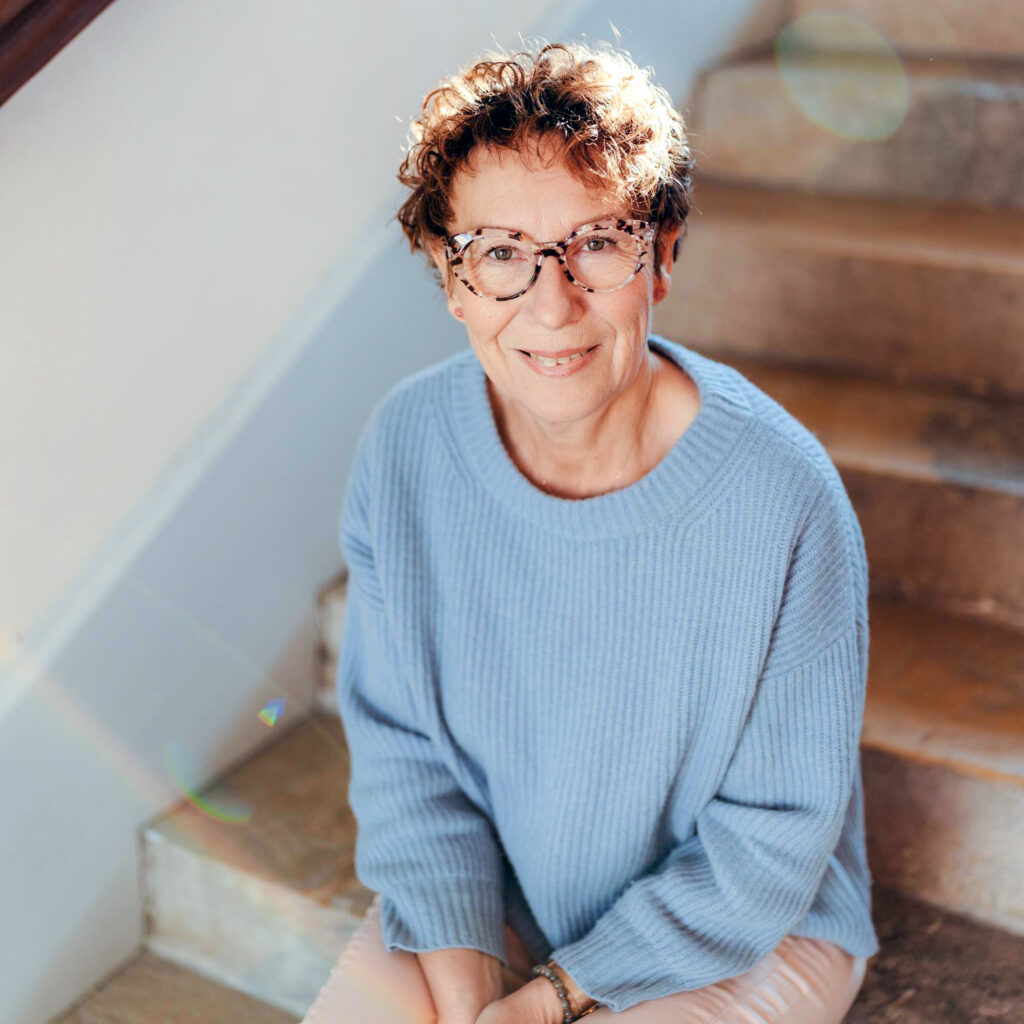 Isabelle Fournier assise sur des marches, rayonnant d’authenticité et de bienveillance, prête à guider avec amour et respect.